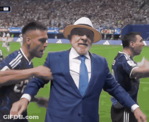 Man In Suit And Tie On Soccer Field Surrounded By Players GIF