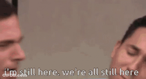 Man In Suit And Tie Saying I'm Still Here, We're All Still Here GIF