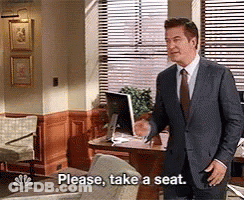 Man In Suit And Tie Saying Please Take A Seat GIF