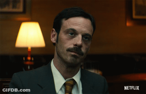 Man In Suit And Tie Sitting At Netflix Sign GIF