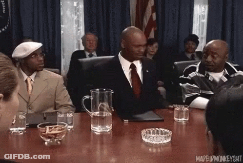 Man In Suit And Tie Sitting At Table In Front Of Crowd GIF