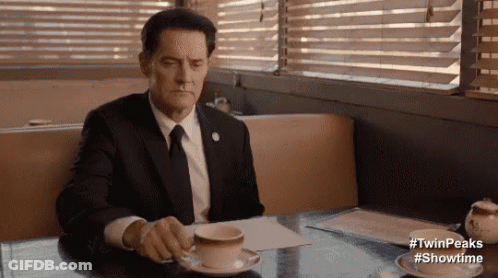Man In Suit And Tie Sitting At Table With Coffee And Saucer GIF