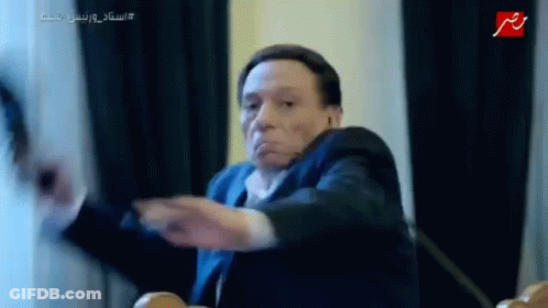 Man In Suit And Tie Sitting At Table With Hands Outstretched GIF