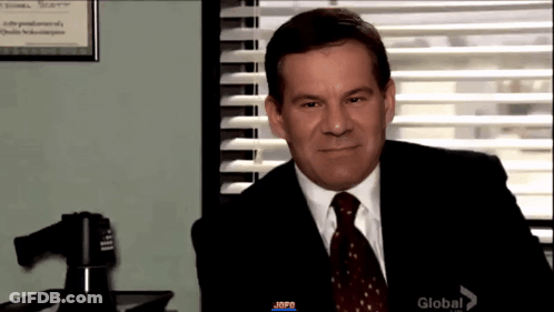 Man In Suit And Tie Sitting By Window With Blinds GIF