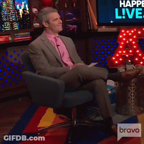 Man In Suit And Tie Sitting In Chair With Legs Crossed On Colorful Rug GIF