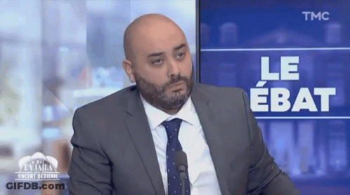 Man In Suit And Tie Sitting In Front Of TMC Screen GIF