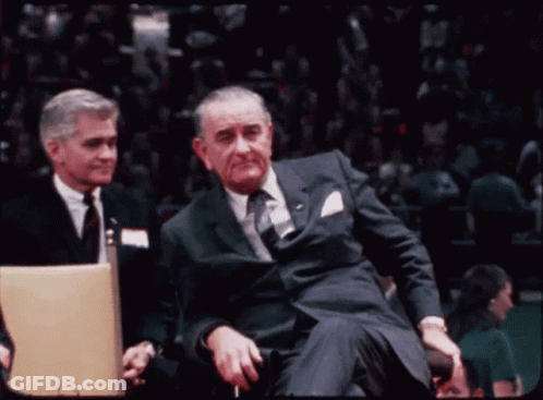 Man In Suit And Tie Sitting In Stadium GIF