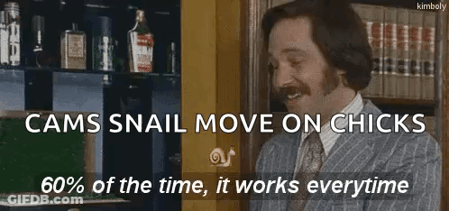 Man In Suit And Tie Smiling In Front Of Bookshelf With Snail GIF
