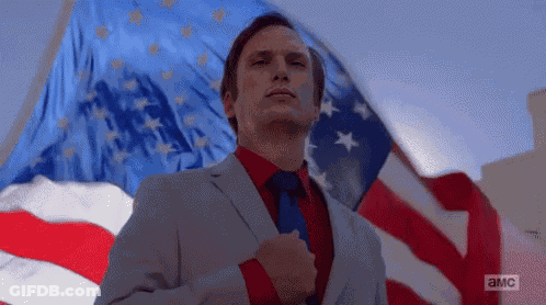 Man In Suit And Tie Standing Before American Flag GIF