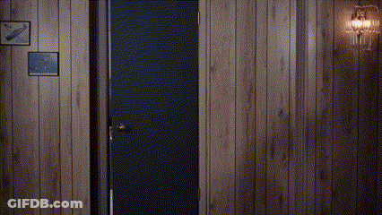 Man In Suit And Tie Standing In Doorway In Wood Paneled Room GIF