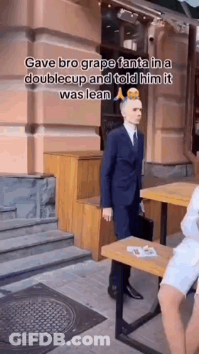 Man In Suit And Tie Standing In Front Of Building And Table GIF