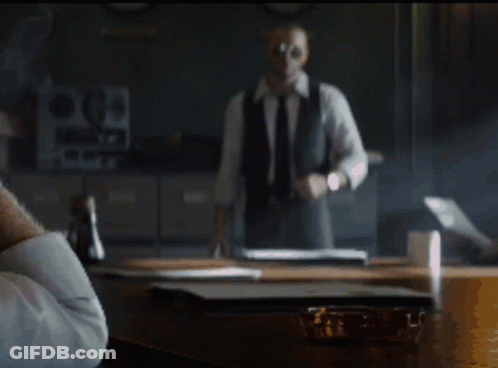 Man In Suit And Tie Standing In Front Of Desk With Letter P GIF