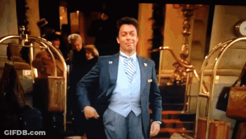 Man In Suit And Tie Standing In Front Of Hotel GIF
