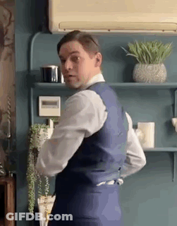 Man In Suit And Tie Standing In Front Of Shelf With Plants GIF