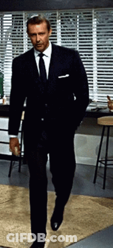 Man In Suit And Tie Walking By Window With Blinds GIF