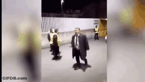 Man In Suit And Tie Walking Down Street Next To Fence GIF