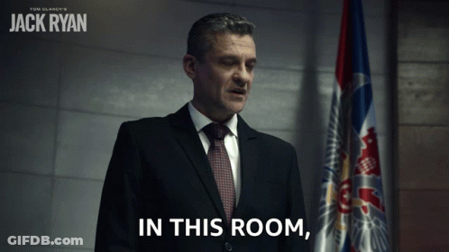 Man In Suit And Tie With Flag Saying In This Room GIF
