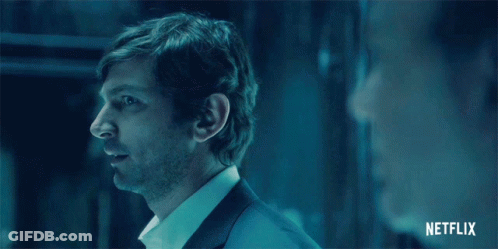 Man In Suit And White Shirt Standing In Dark Room With Netflix Logo GIF