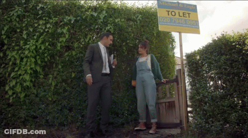 Man In Suit And Woman In Overalls Next To To Let Sign GIF