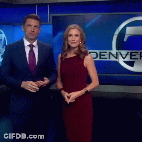 Man In Suit And Woman In Red Dress In Front Of Denver Sign GIF