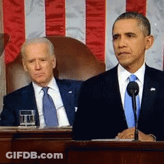 Man In Suit At Microphone With Seated Man GIF