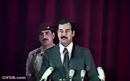 Man In Suit At Microphones With Military Behind GIF
