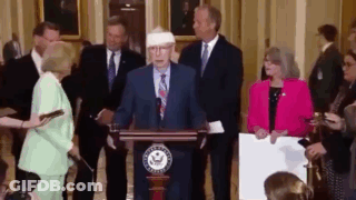 Man In Suit At Podium With Bandaged Head GIF