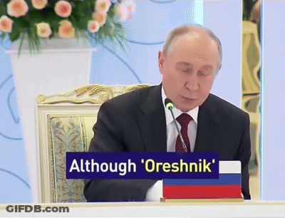 Man In Suit At Table With Sign Although Oreshnik GIF