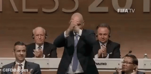 Man In Suit Covering Face While Men Applaud GIF