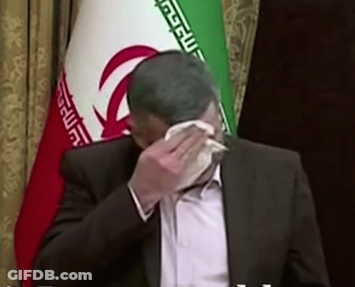 Man In Suit Covering Face With Napkin Near Iranian Flag GIF