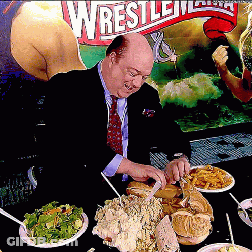 Man In Suit Eating In Front Of Wrestlemania Sign GIF