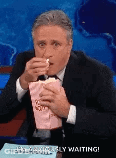 Man In Suit Eating Popcorn At Table GIF