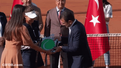 Man In Suit Giving Tennis Racket To Woman In White Visor GIF