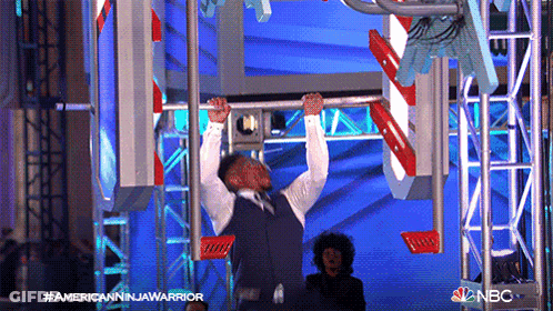 Man In Suit Hanging Upside Down On Bar With NBC Logo GIF