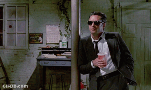 Man In Suit Holding Cup Leaning On Pole GIF