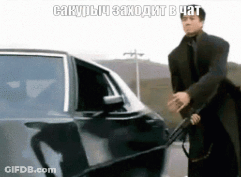 Man In Suit Holding Gun In Front Of Car With Foreign Caption GIF