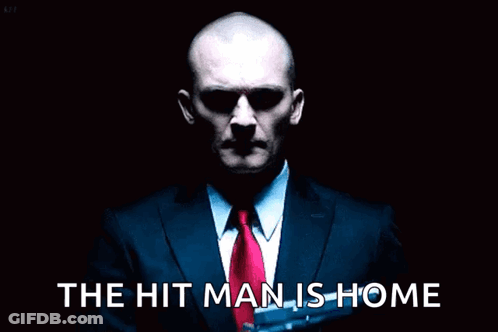 Man In Suit Holding Gun Saying The Hit Man Is Home GIF