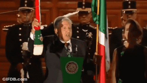 Man In Suit Holding Mexican Flag At Podium GIF