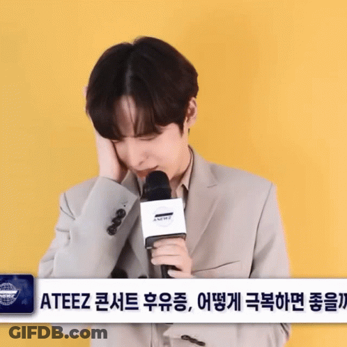 Man In Suit Holding Microphone In Front Of ATEEZ Sign GIF
