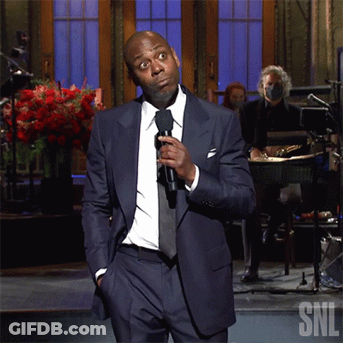 Man In Suit Holding Microphone In Front Of SNL Logo GIF