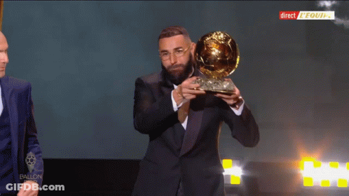 Man In Suit Holding Trophy In Front Of Direct Equipe Screen GIF