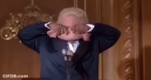 Man In Suit Holds Cloth Over Head Speaking Into Mic GIF