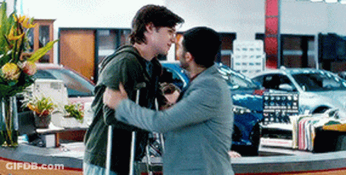 Man In Suit Hugging Man With Crutches In Car Dealership GIF