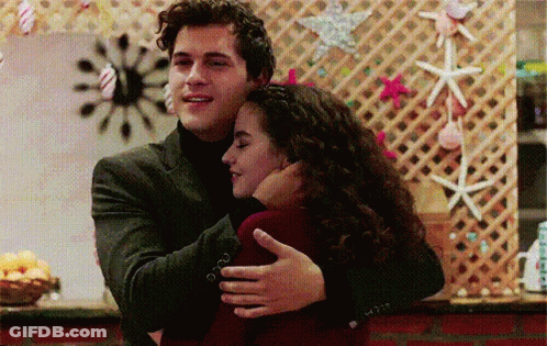 Man In Suit Hugging Woman In Front Of Seashell Wall GIF
