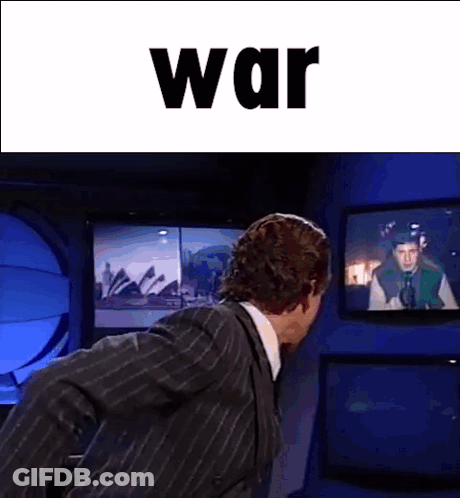Man In Suit In Front Of TV Saying War GIF