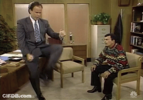 Man In Suit Jumping On Chair Beside Seated Man GIF
