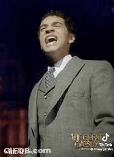 Man In Suit Laughing In Front Of The Great Gatsby Sign GIF