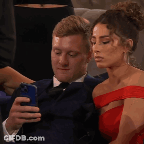 Man In Suit Looking At Phone Woman In Red Dress Looking At Him GIF