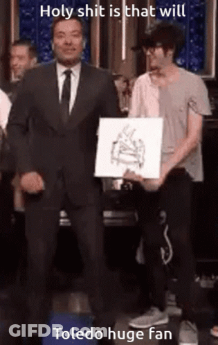 Man In Suit Next To Man Holding Toledo Huge Fan Paper GIF