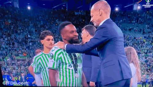 Man In Suit Next To Man In Green White Jersey Saying Re GIF